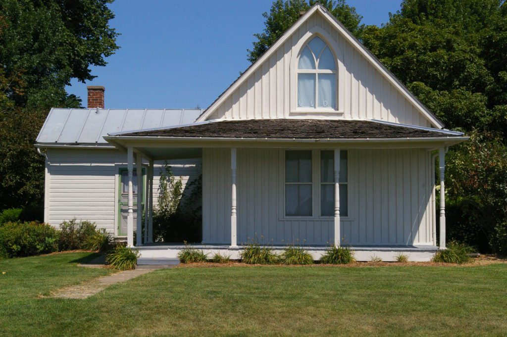White facade with covered porch and curved window at the American Gothic House in Eldon, Iowa