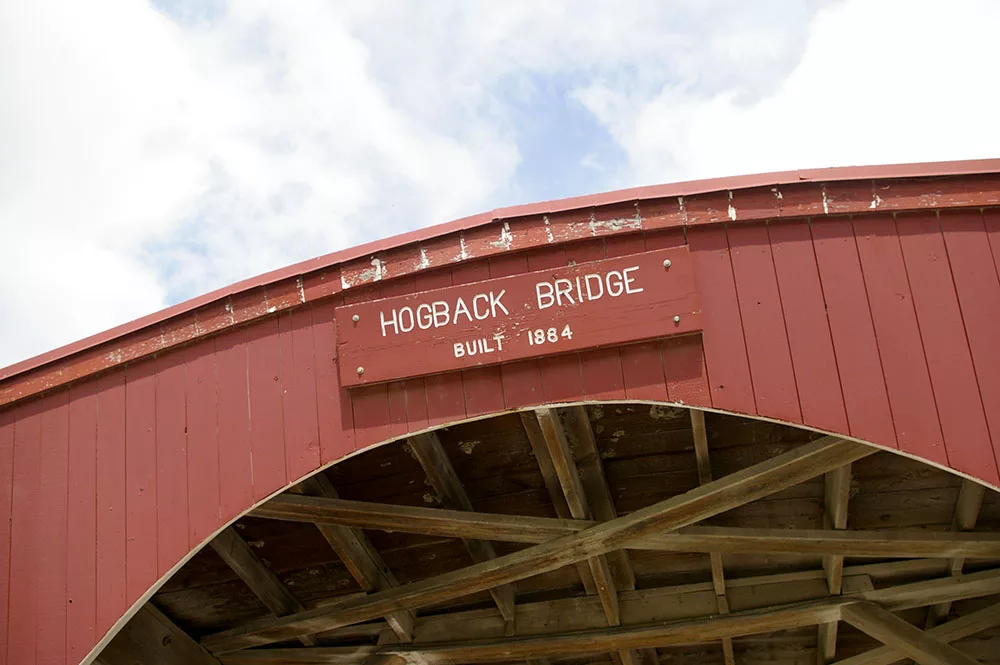 Red painted exterior with sign with white lettering reading "Hogback Bridge: Built 1884" on Hogback Covered Bridge, one of the six remaining Bridges of Madison County near Winterset, Iowa