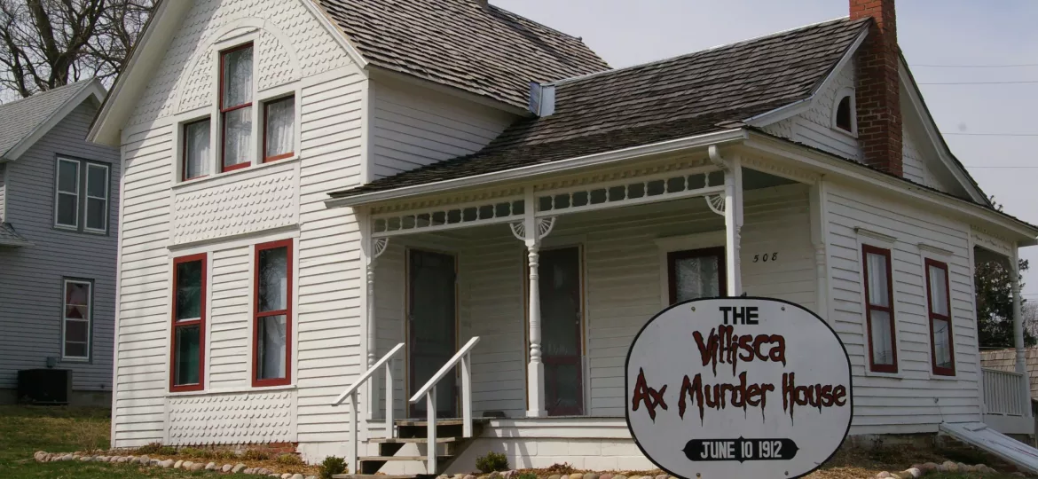 White farmhouse with red trim and sign that says Villisca Ax Murder House in Villisca, Iowa