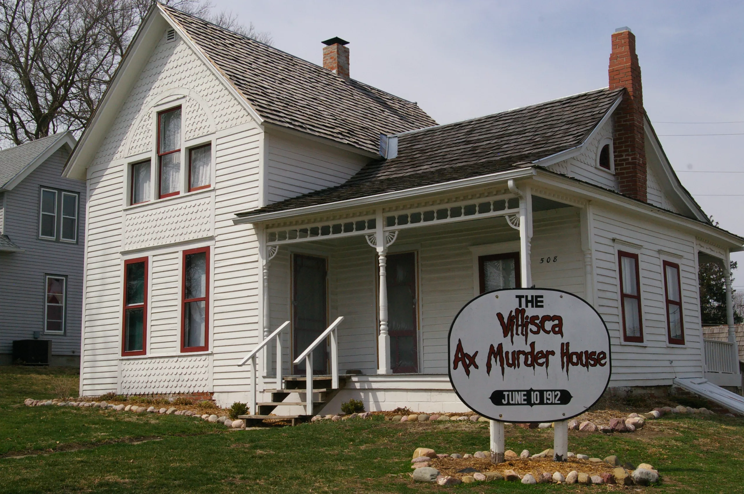 White farmhouse with red trim and sign that says Villisca Ax Murder House in Villisca, Iowa