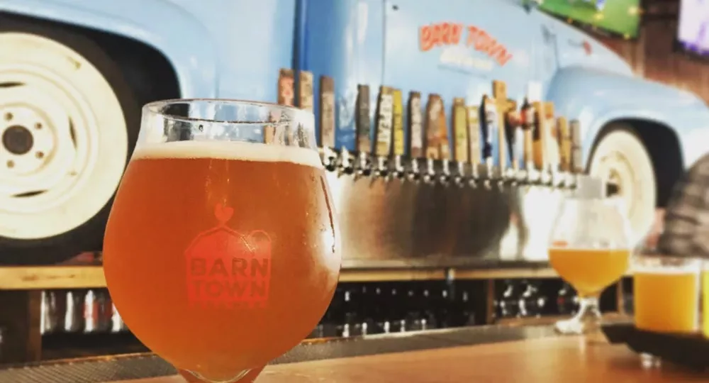 Beer in a tulip glass reading "Barn Town Brewing" on a wood bar in front of a wall with blue pickup truck backer and beer taps at Barn Town Brewing near Des Moines, Iowa