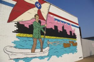 Mural of man crossing a river holding the Wichita flag in the Douglas Design District of Wichita, Kansas