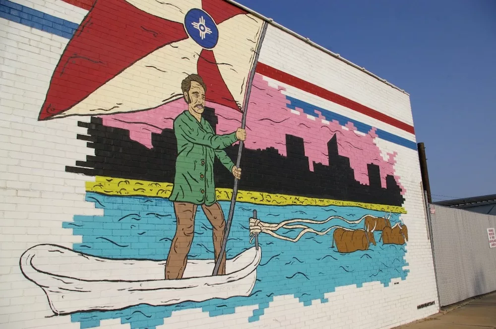 Mural of man crossing a river holding the Wichita flag in the Douglas Design District of Wichita, Kansas