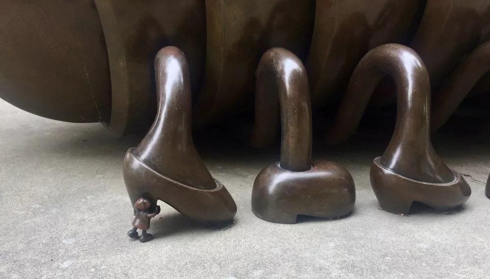 Detail of small person holding up foot of bronze sculpture named Millie the Millipede outside of the Ulrich Museum of Art on the Wichita State campus in Wichita, Kansas