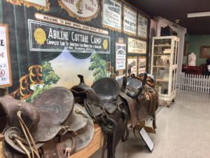 Display of leather saddles in front of information about the Abilene Cattle Company at the Dickinson County Heritage Center in Abilene, Kansas