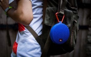 Blue waterproof JBL Clip speaker attached to a backpack