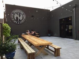 Black exterior of building with long wooden picnic table and strand lighting at Nortons Brewing Company in Wichita, Kansas