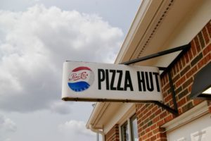 White sign reading "Pizza Hut" with red, white, and blue Pepsi logo on the exterior of a brown brick building on the Wichita State University campus in Wichita, Kansas