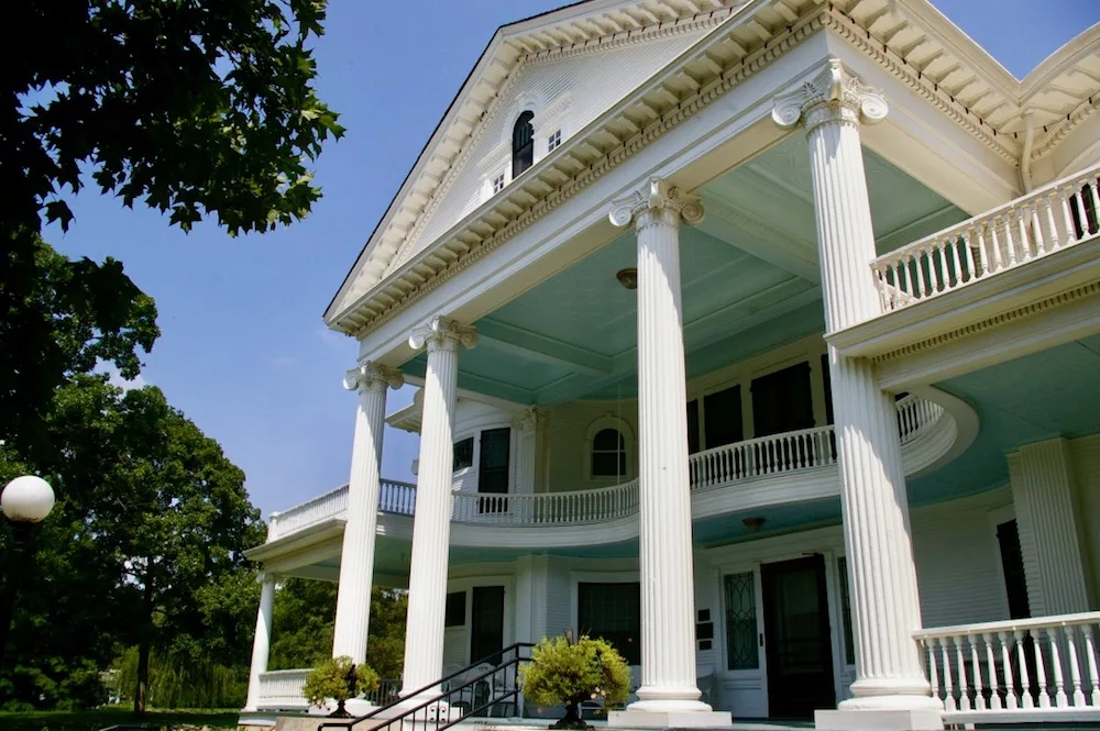 Exterior of home with tall white columns and large wraparound porch painted with a baby blue ceiling at the Seelye Mansion in Abilene, Kansas