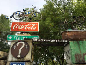 Bicycle on top of CocaCola sign on top of cement pillar with various signs and placards at the outdoor art installation, Rancho Deluxe, in Mason City, Iowa