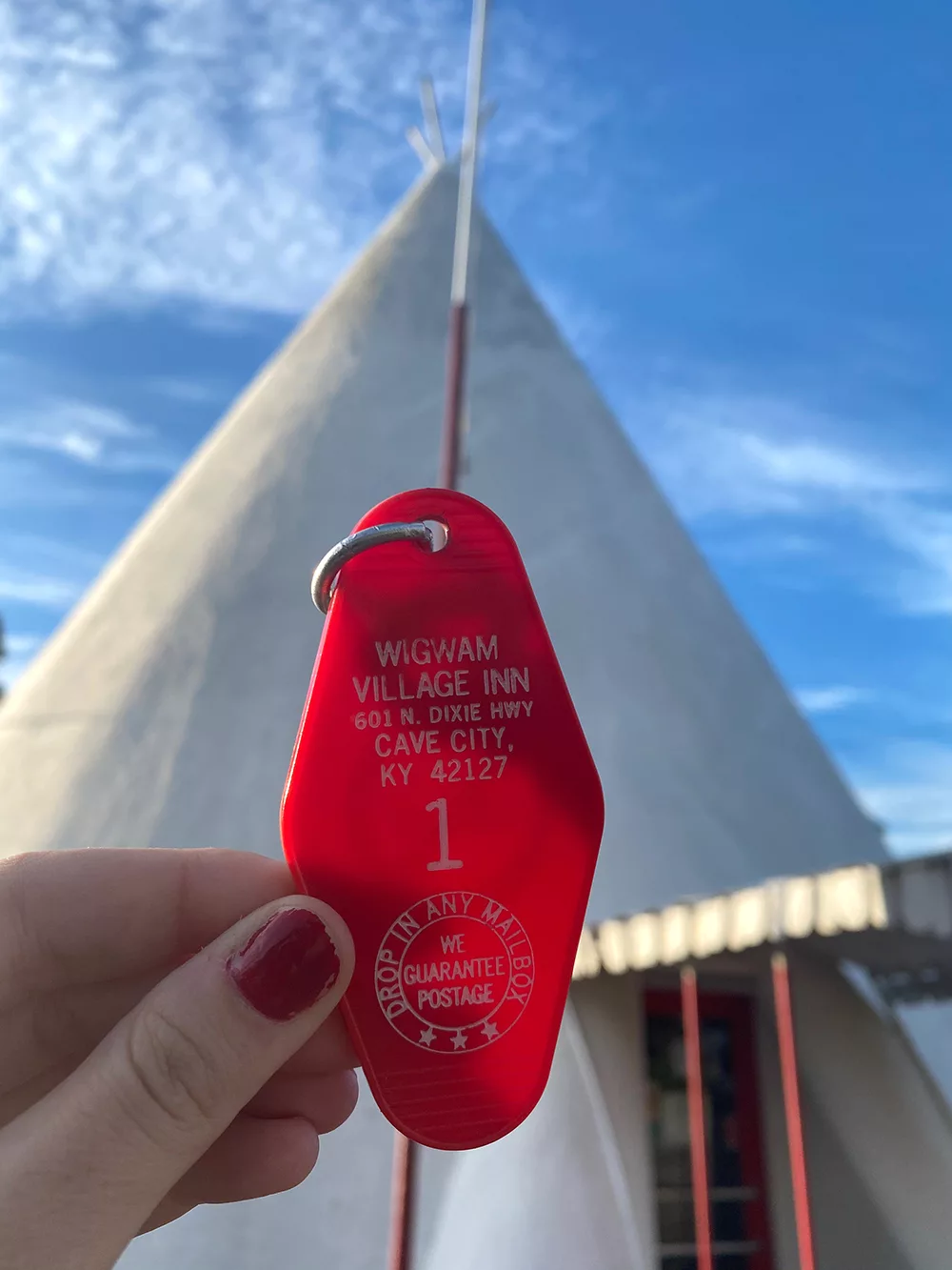 Red hotel key tag from the Wigwam Village Inn #2 in front of large concrete teepee in Cave City, Kentucky