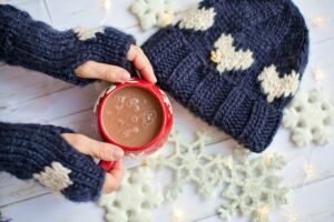 Hands wearing navy gloves holding a red mug of hot cocoa against a white snowflake background | Olio in Iowa's 2020 Holiday Gift Guide