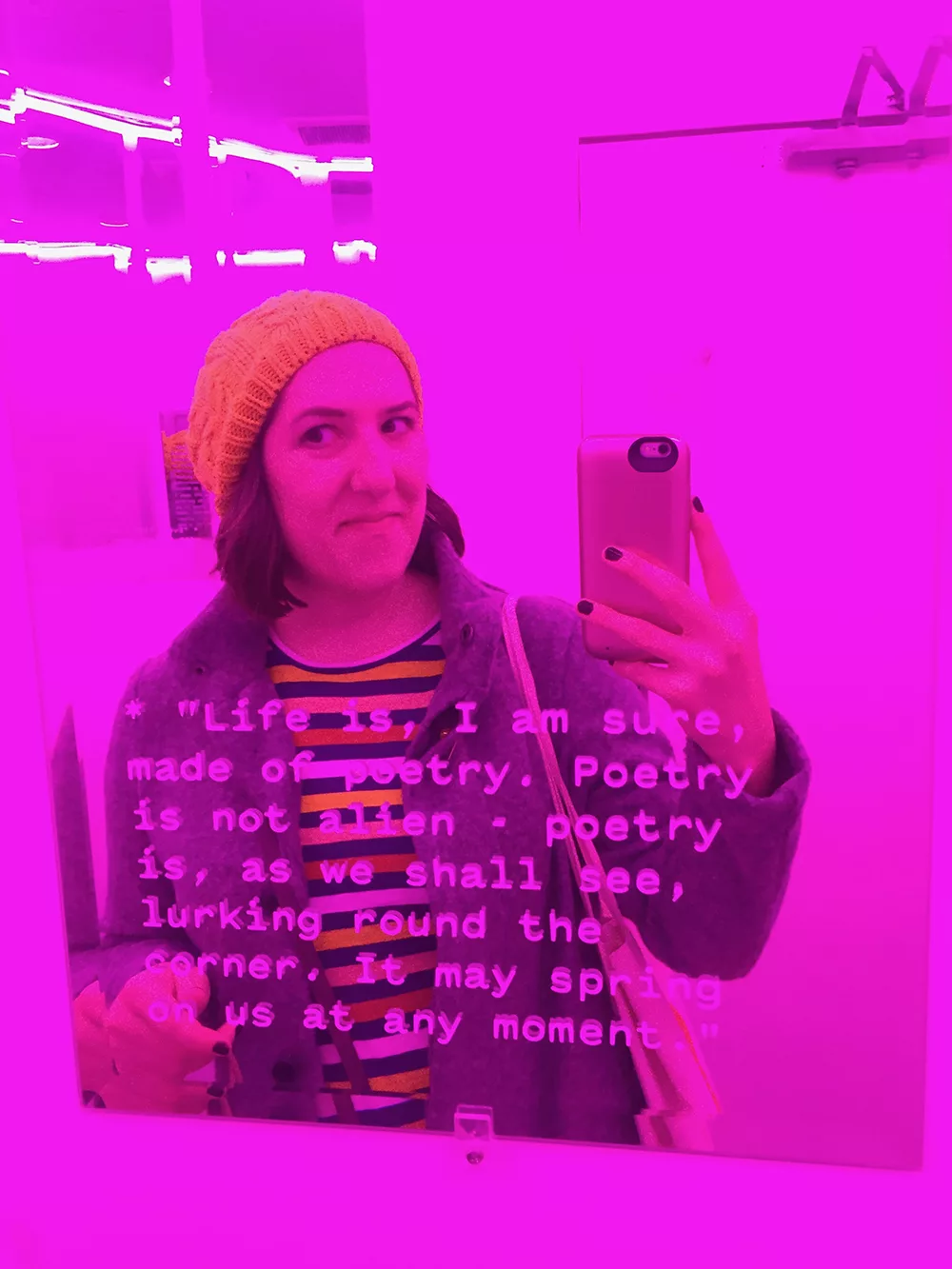 Women taking a photo in a mirror in a pink neon bathroom with quotes by Jorge Louis Borges on the mirrors