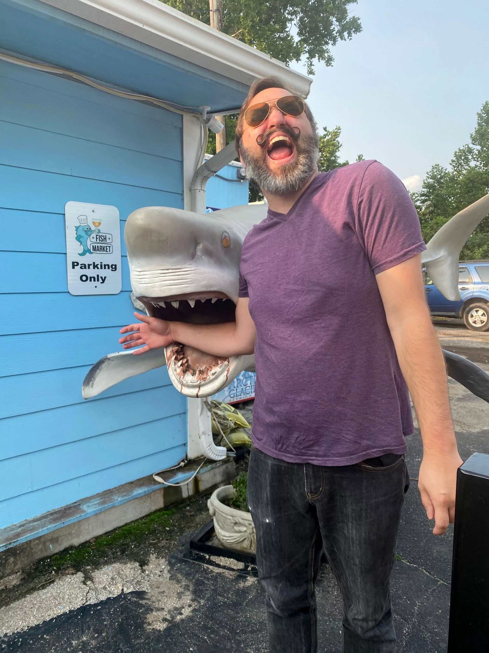 Man with mustache pretending to be bitten by shark statue at The Fish Market in Liberty, Missouri