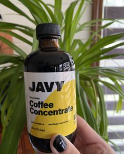 Hand holding bottle of Javy Coffee Concentrate in front of houseplant