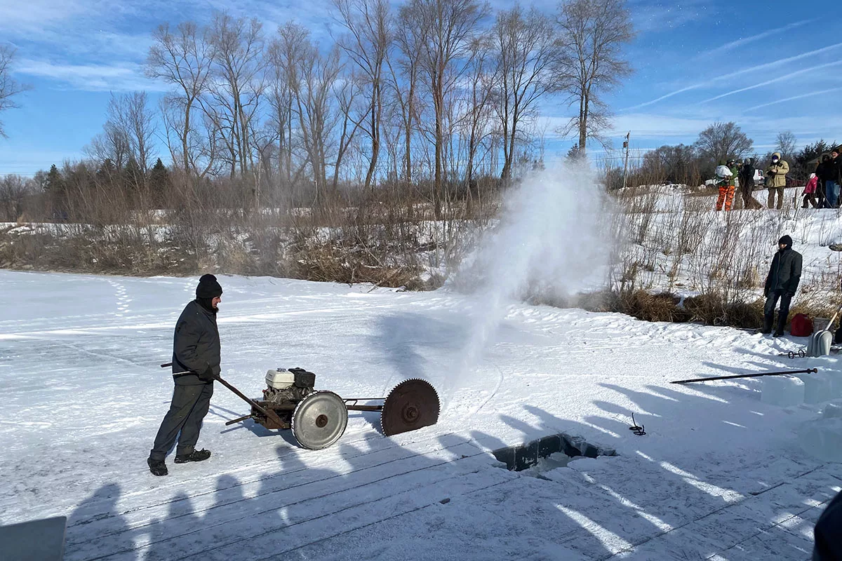 Man using gas-powered saw to cut ice during an ice harvesting presentation at the 2022 Ice Harvest Festival in Cedar Falls, Iowa