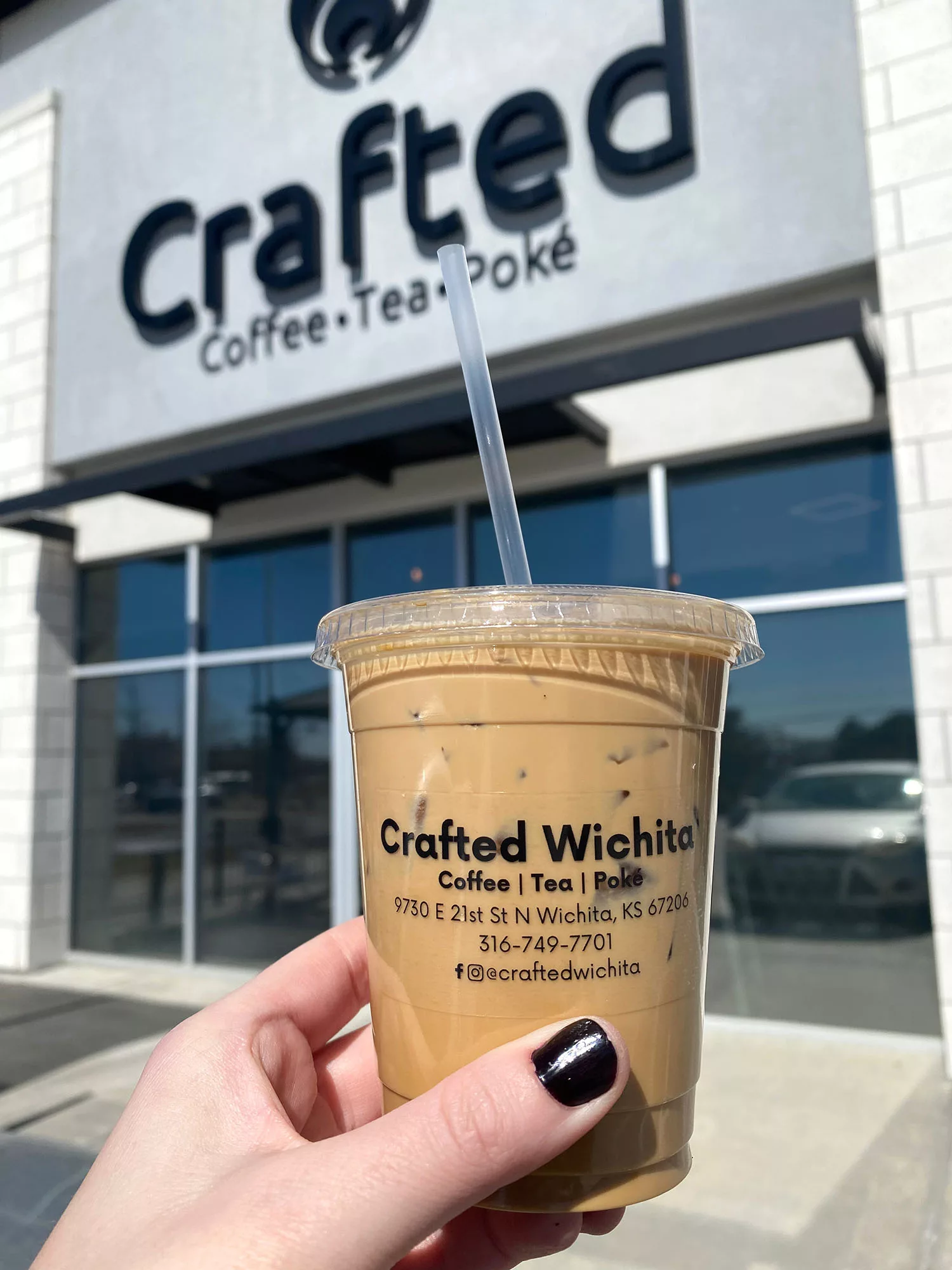 Hand holding Thai iced coffee in front of sign for Crafted in Wichita, Kansas