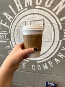 Hand holding coffee cup in front of mural at Fairmount Coffee Co. in Wichita, Kansas