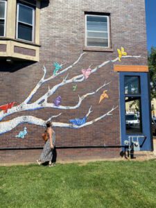 Person standing in front of mural of tree with paper cranes in Janesville, Wisconsin