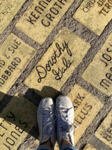 White pair of sneakers against Yellow Brick Road that says Dorothy Gale at Dorothy's House & Land of Oz in Liberal, Kansas