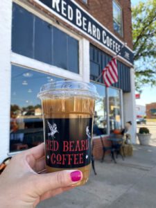 Hand holding coffee cup with Red Beard Coffee on it in front of Red Beard Coffee in Dodge City, Kansas