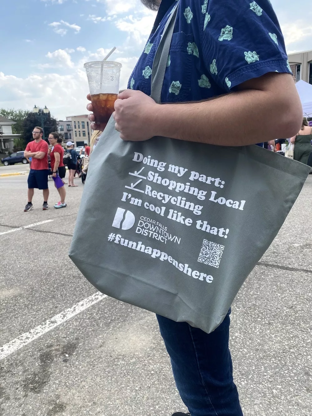 Person holding iced coffee and reusable grocery bag at the Cedar Falls Farmers' Market in Cedar Falls, Iowa