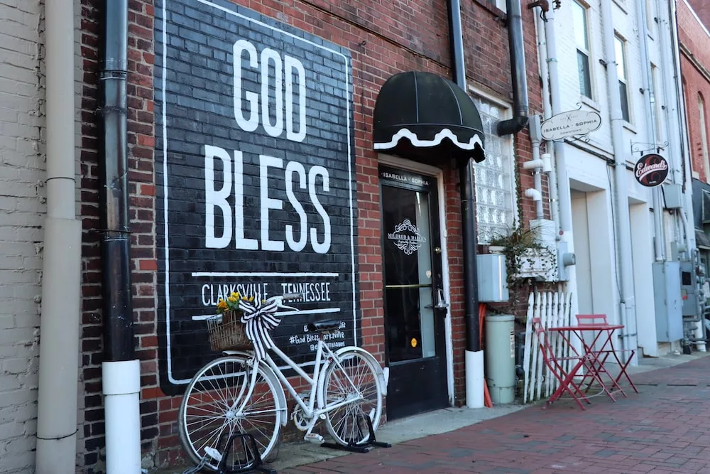 God Bless Clarksville mural with white bike in front of it in downtown Clarksville, Tennessee